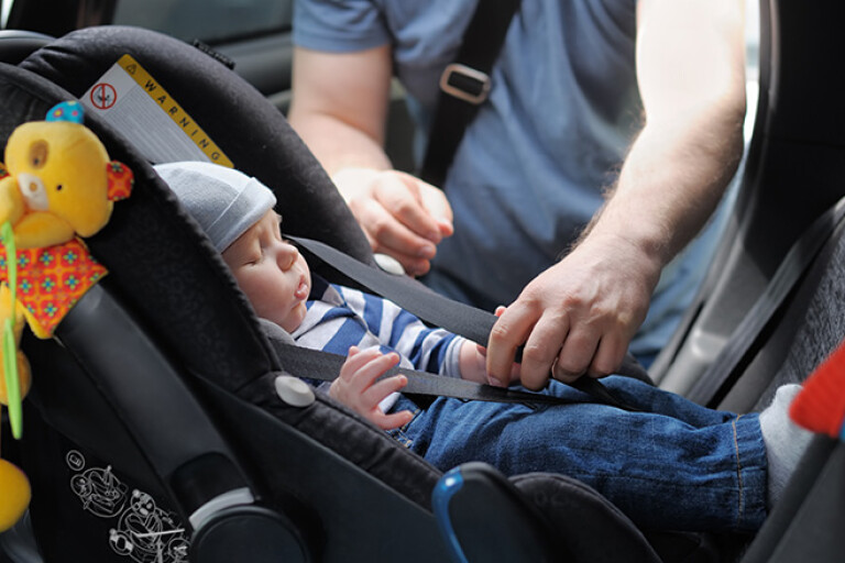 Father putting baby into rear facing car child seat